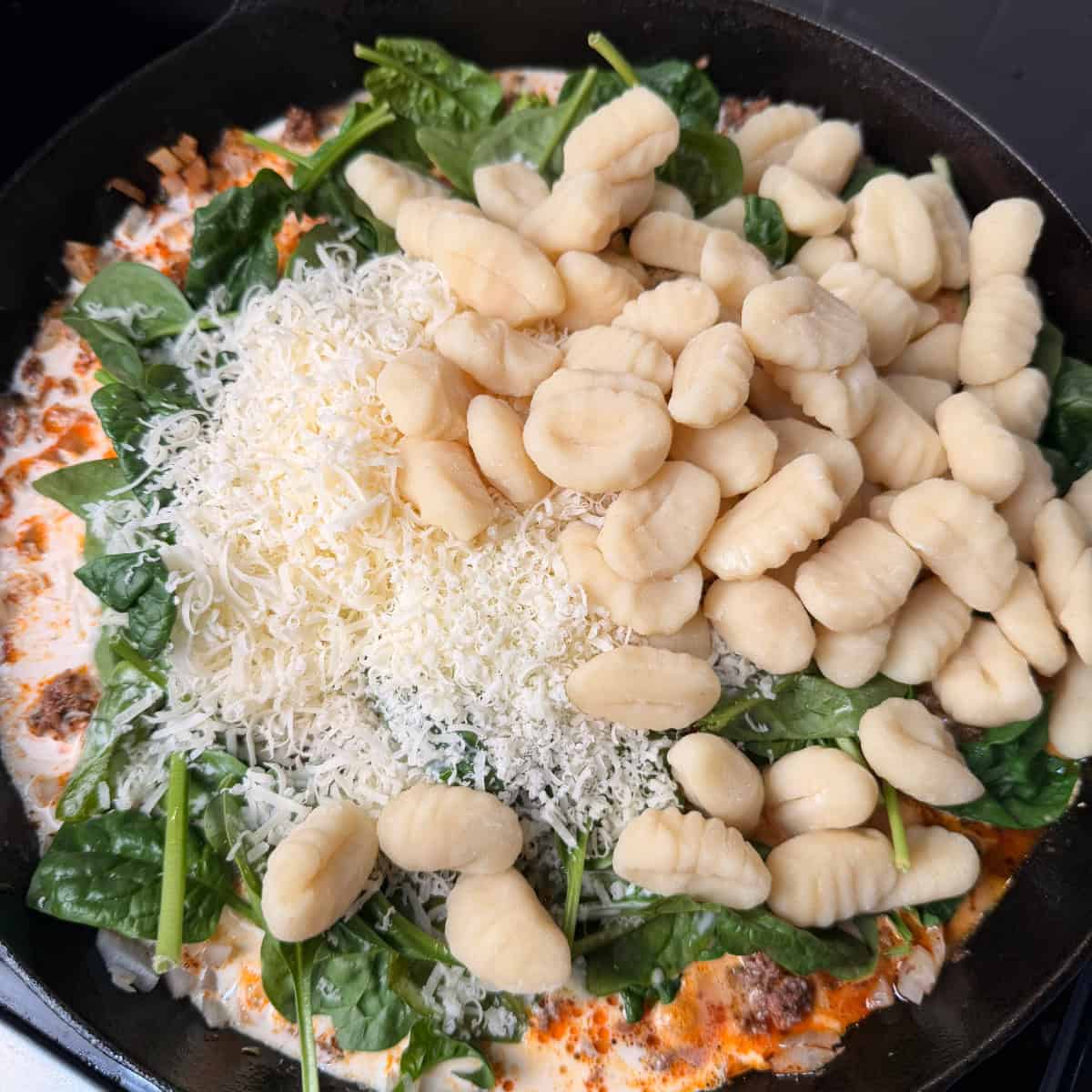 Ground beef, spinach, tomatoes, gnocchi, Parmesan cheese in skillet