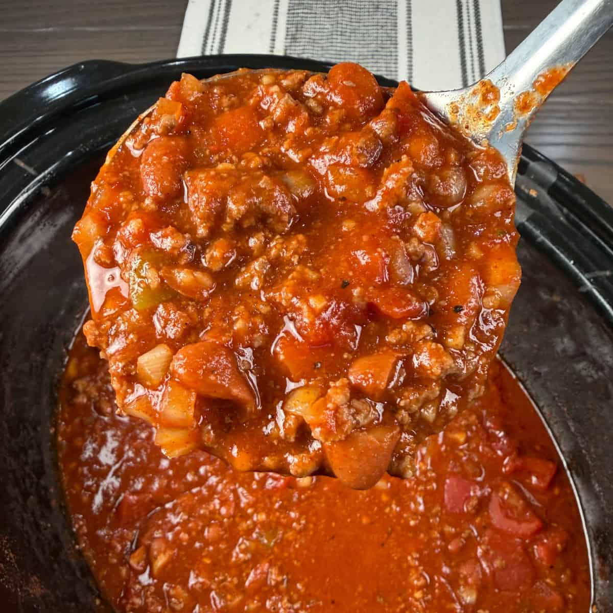 Chili in a ladle getting scooped out of crockpot