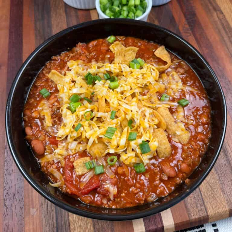 Bowl of Chili topped with shredded cheese, Fritos, and green onions
