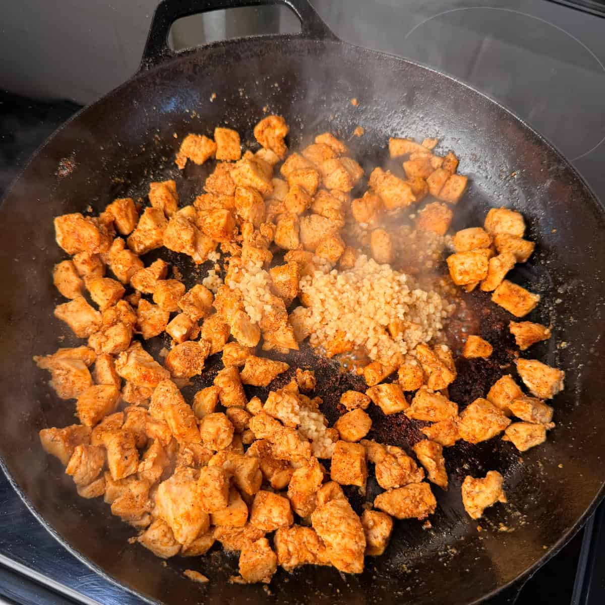 Chicken cooking in skillet with minced garlic