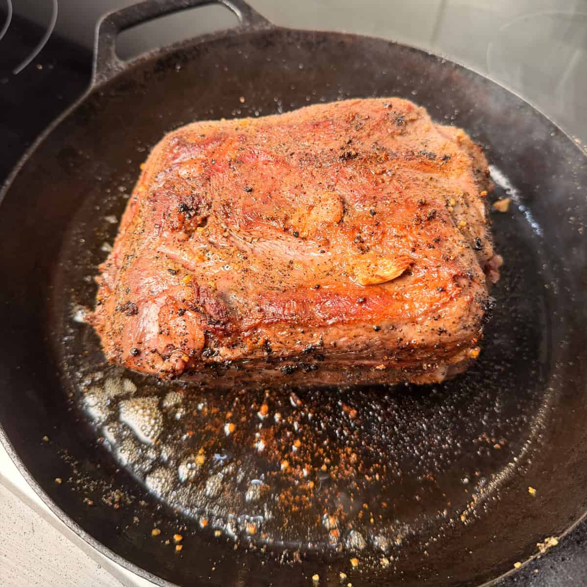 Seasoned chuck roast searing in cast iron skillet