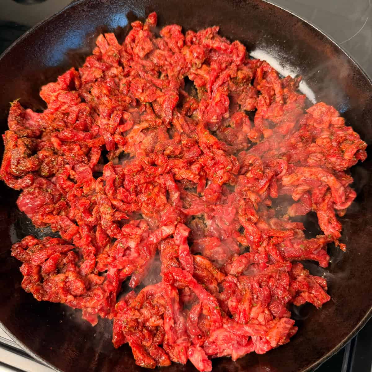 Thin slices of Strip Steak in Cast iron skillet and seasoned with taco seasoning