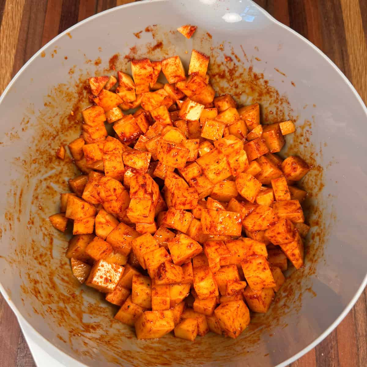 Chopped potatoes in bowl seasoned with oil and salt, pepper, garlic powder, and paprika