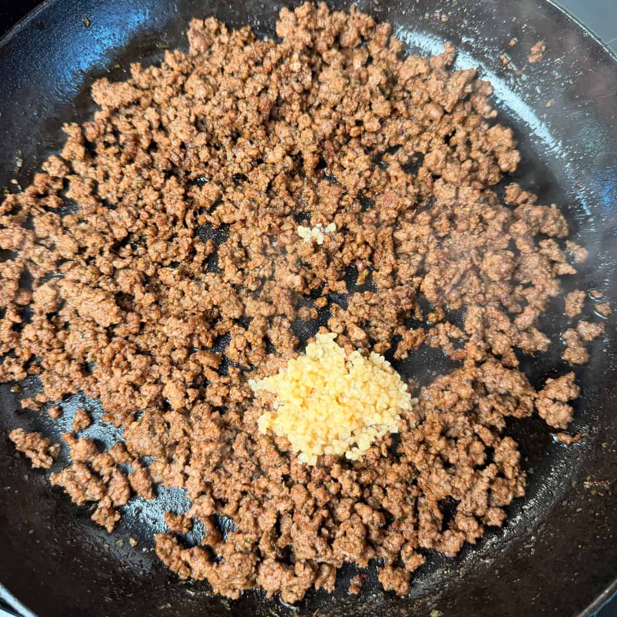 Seasoned ground beef in cast iron skillet with minced garlic