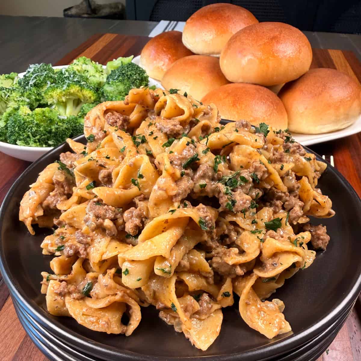 Plated ground beef stroganoff with broccoli and rolls