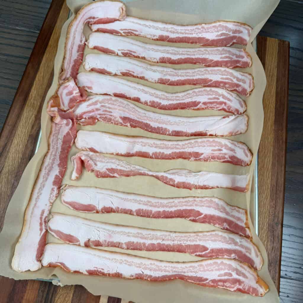 Uncooked bacon on sheet pan lined with parchment paper
