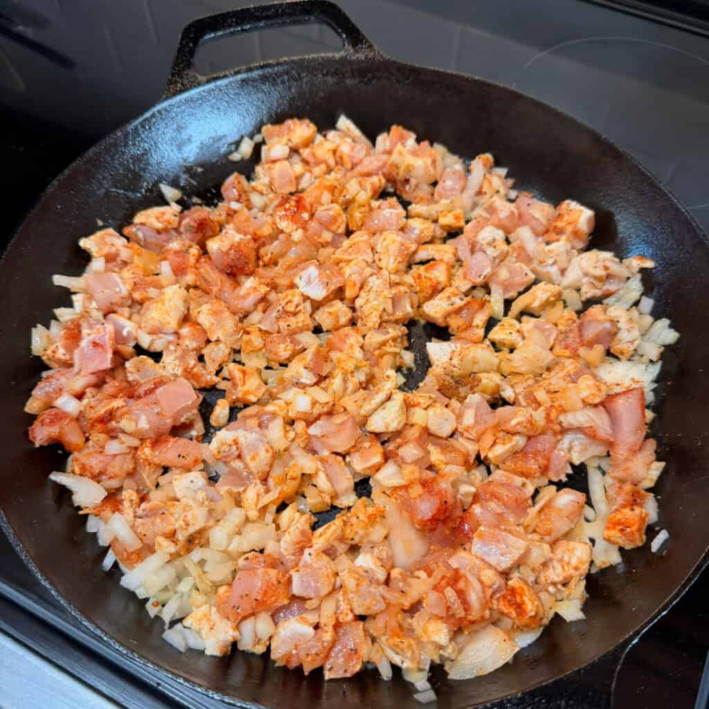 Cast iron skillet with cooking chicken, onion, and seasonings