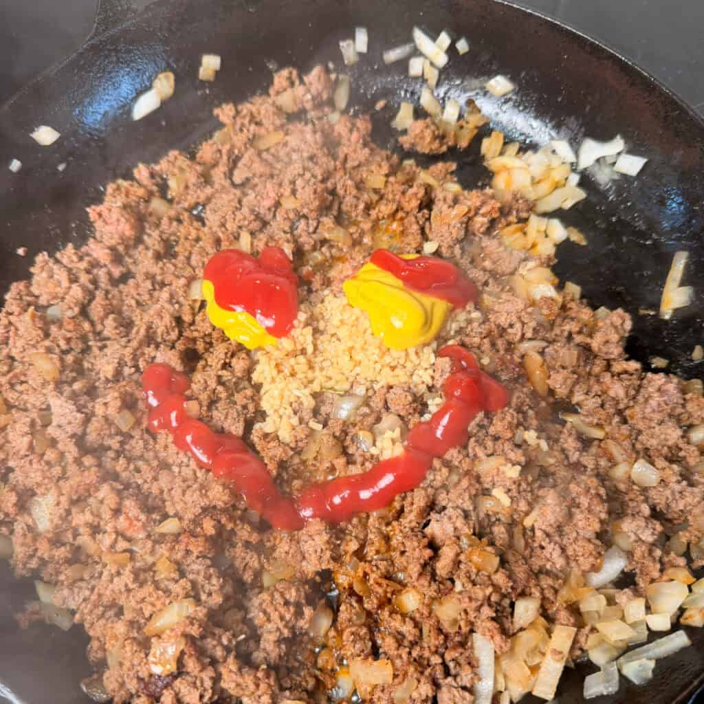 Browned beef, garlic, ketchup, and mustard in skillet