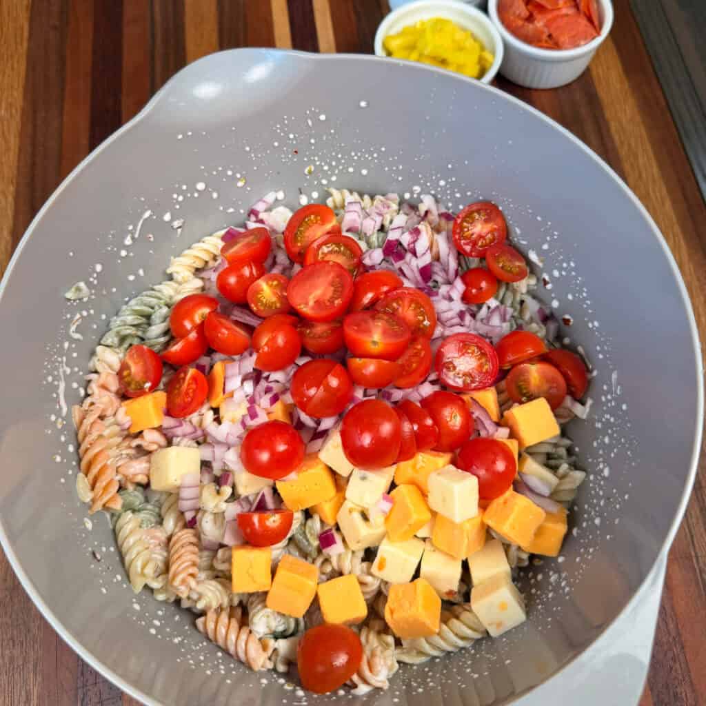 Making the pasta salad in bowl with dressing, pasta, onions, tomatoes, and cheese cubes
