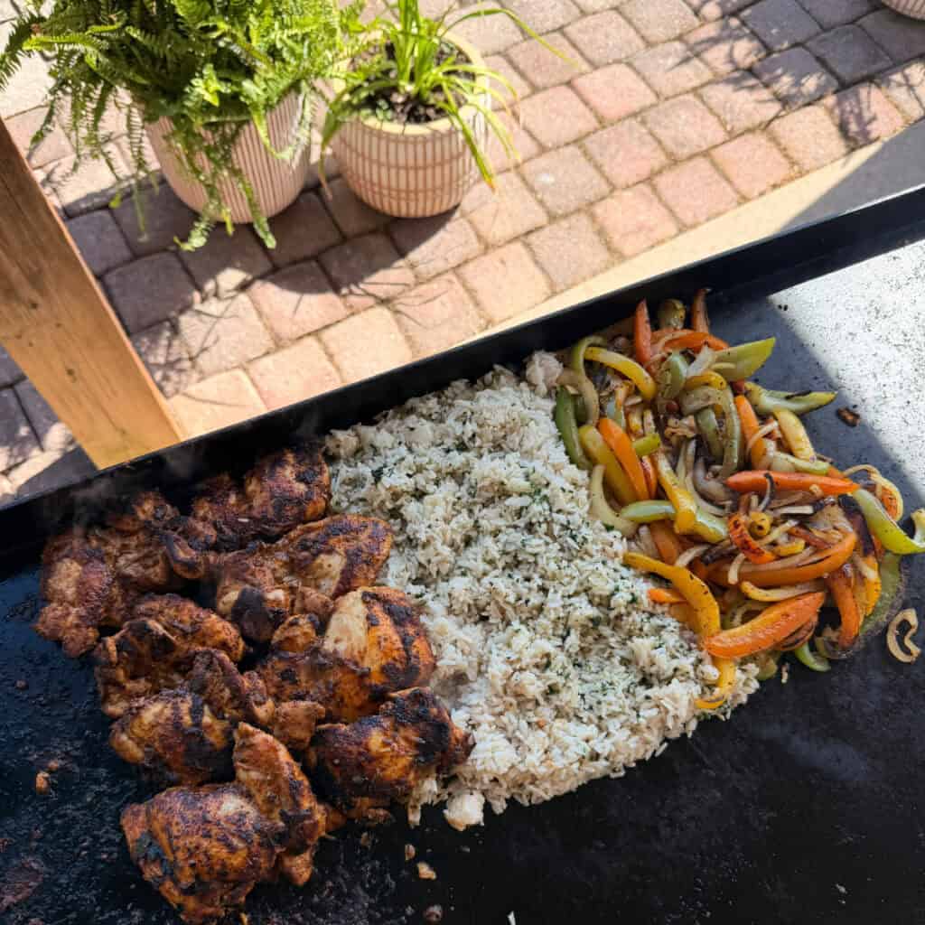 Chicken thighs, rice, peppers, and onion cooking on a griddle