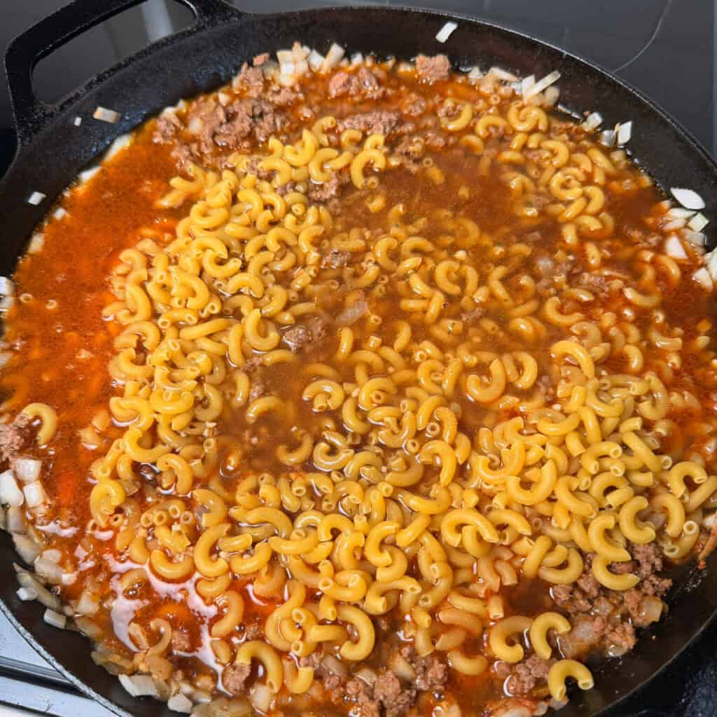 uncooked pasta, beef, broth, onions, seasonings in a skillet