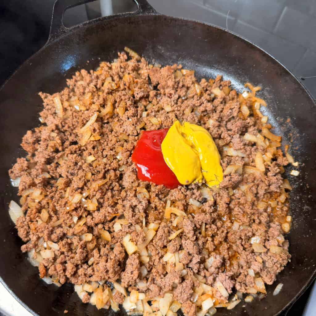 Browned beef with ketchup, mustard, and pickle juice in skillet