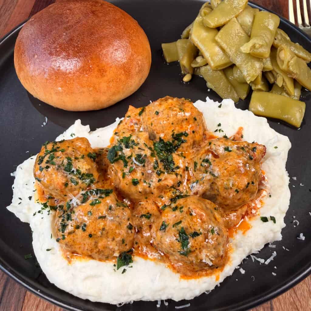Plated Crockpot Marry Me Meatballs over mashed potatoes with green beans and roll