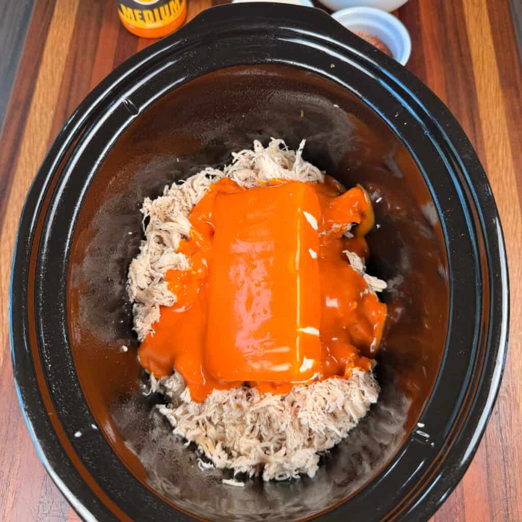 Crockpot with shredded chicken, cream cheese, and buffalo sauce