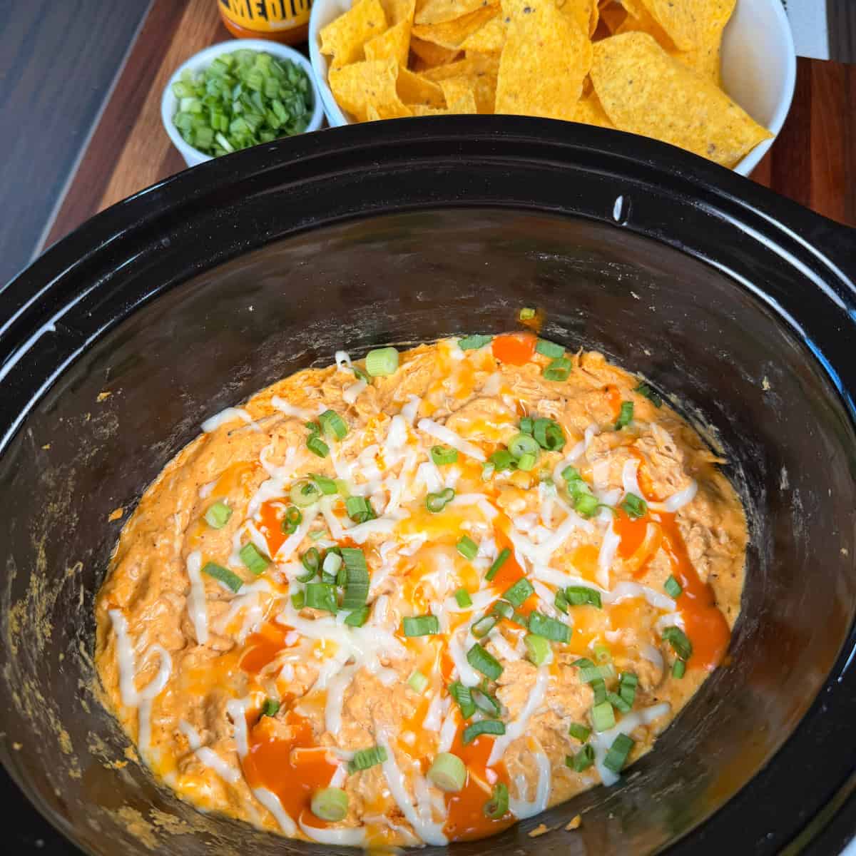Crockpot of Buffalo Chicken dip with tortilla chips and green onions