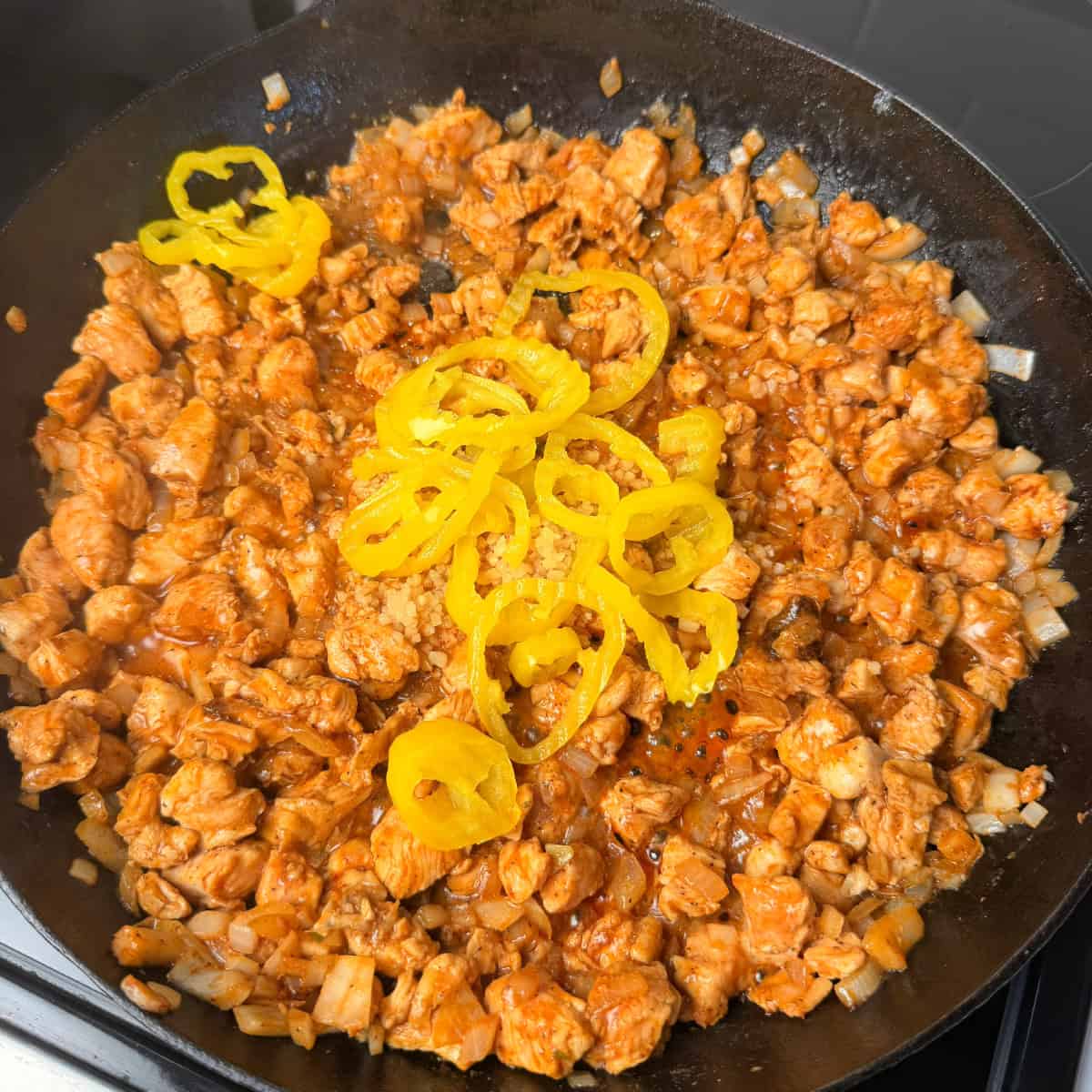 Cooked chicken and onions in skillet with banana pepper rings