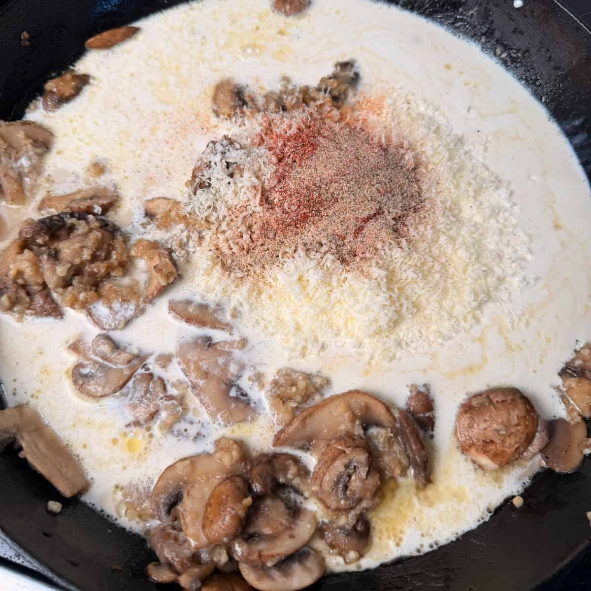 cooked mushrooms, roux, with beef broth, heavy cream, Parmesan cheese and seasonings in cast iron skillet
