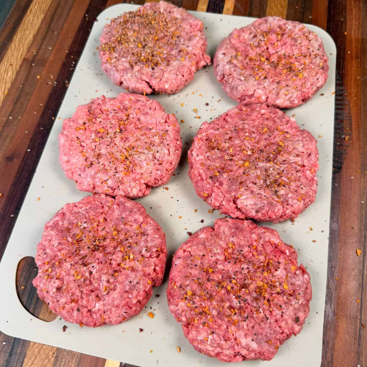 Seasoned burger patties on cutting board