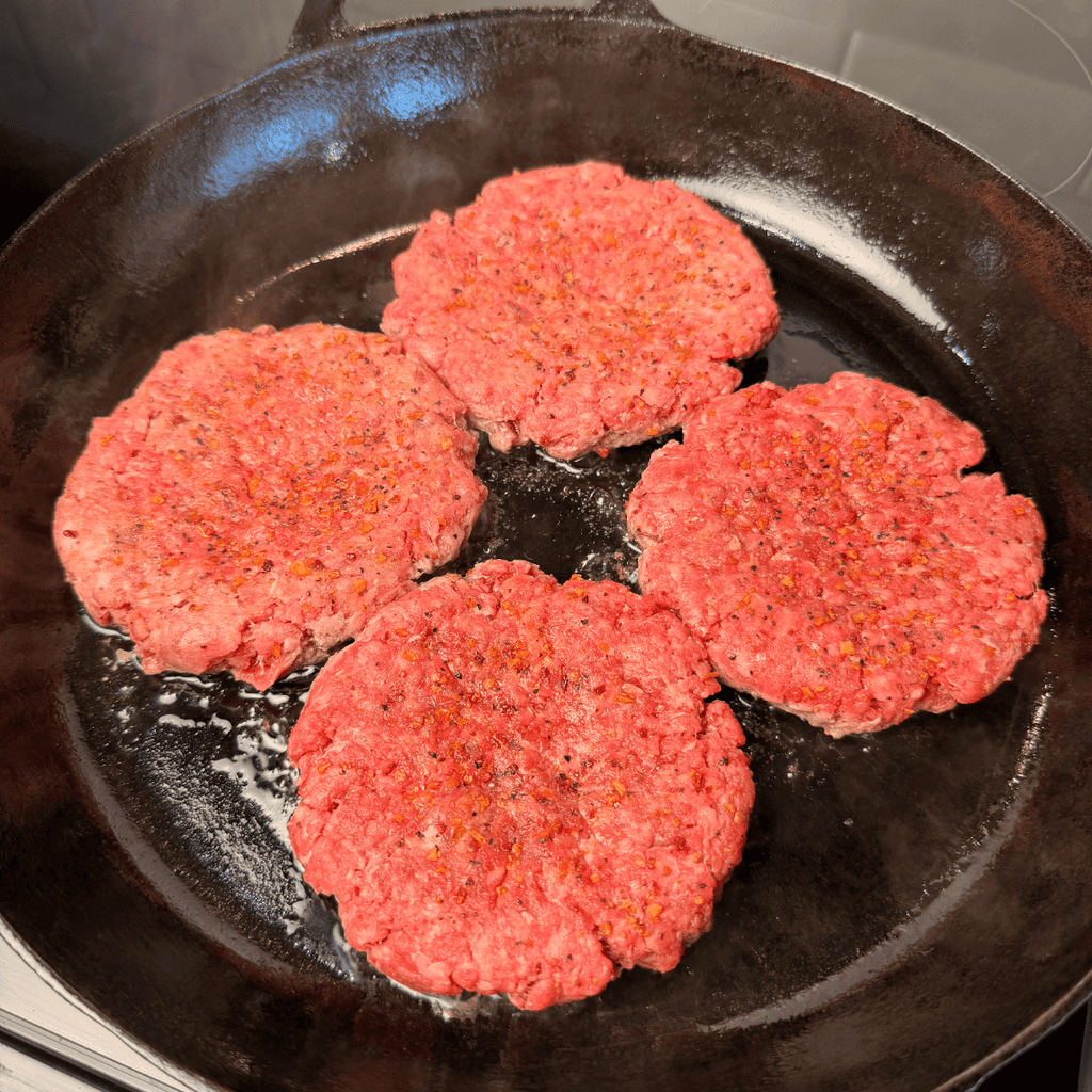 4 raw seasoned burger patties in cast iron skillet