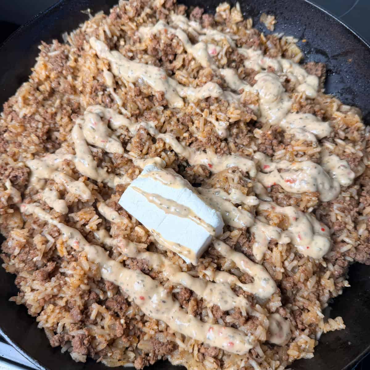 Cooked beef and rice with Parmesan garlic sauce and cream cheese added to cast iron skillet